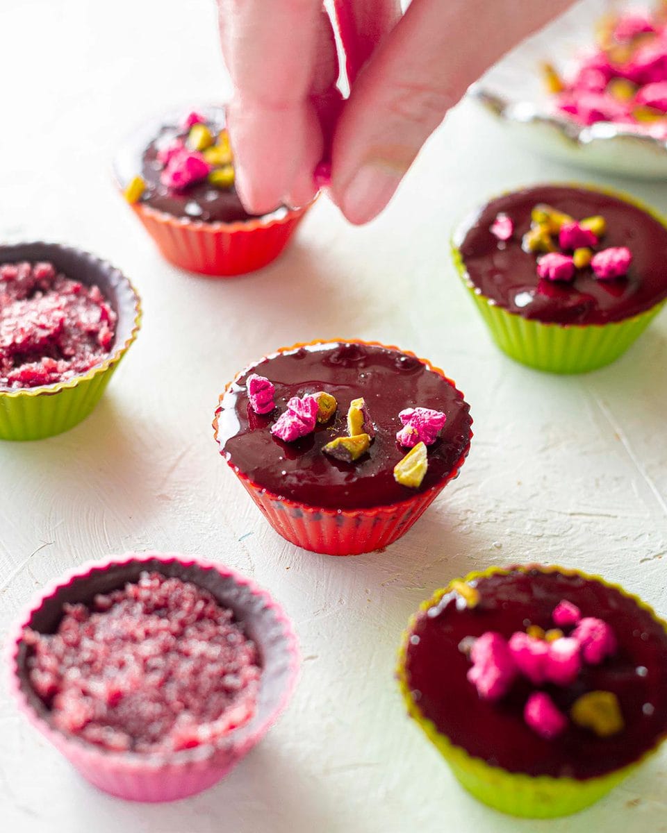 Sprinkling freeze dried raspberries and pistachios on unset chocolate cup.