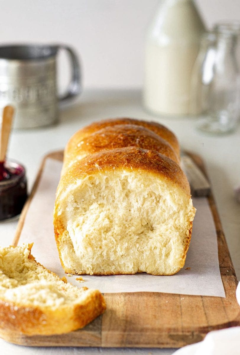 Vegan brioche french bread on chopping board. Slice cut off showing golden and soft interior. The board is surrounded by brioche accompaniments such as jam