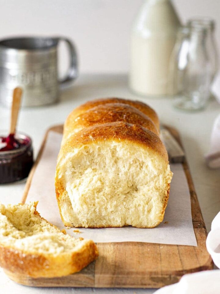 Vegan brioche french bread on chopping board. Slice cut off showing golden and soft interior. The board is surrounded by brioche accompaniments such as jam