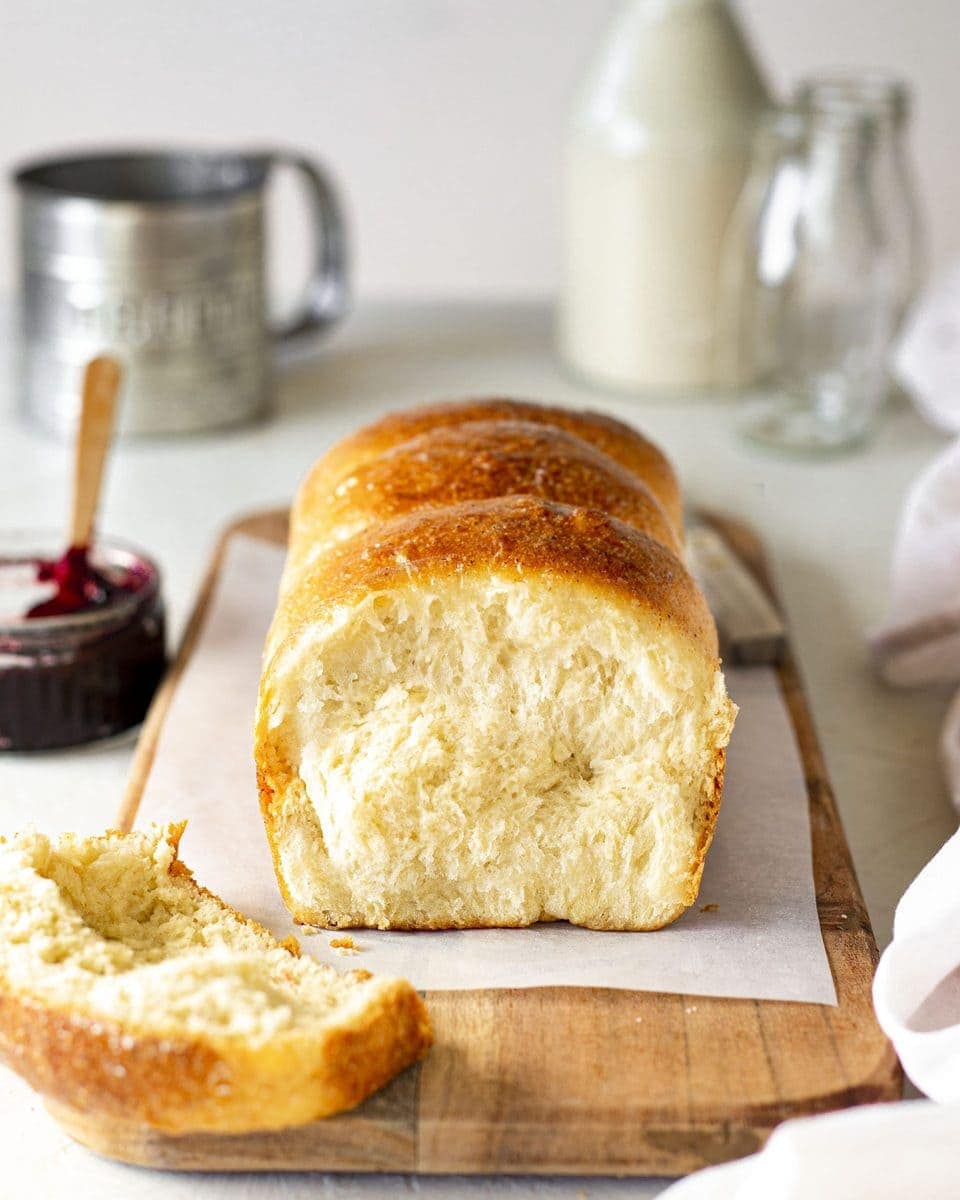 Vegan brioche french bread on chopping board. Slice cut off showing golden and soft interior. The board is surrounded by brioche accompaniments such as jam