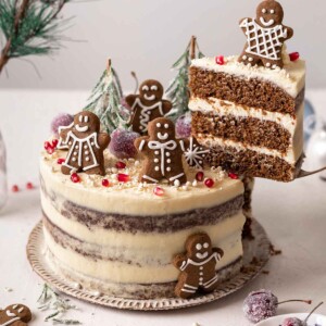 Decorated 3-layered gingerbread cake with a slice lifted up revealing layers of cake and frosting.