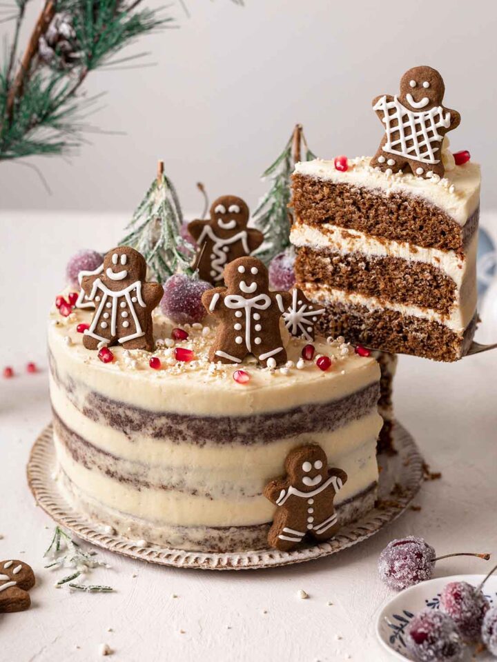 Decorated 3-layered gingerbread cake with a slice lifted up revealing layers of cake and frosting.