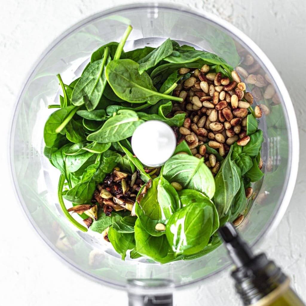 Spinach, basil, pine nuts, garlic and olive oil in food processor for pesto.