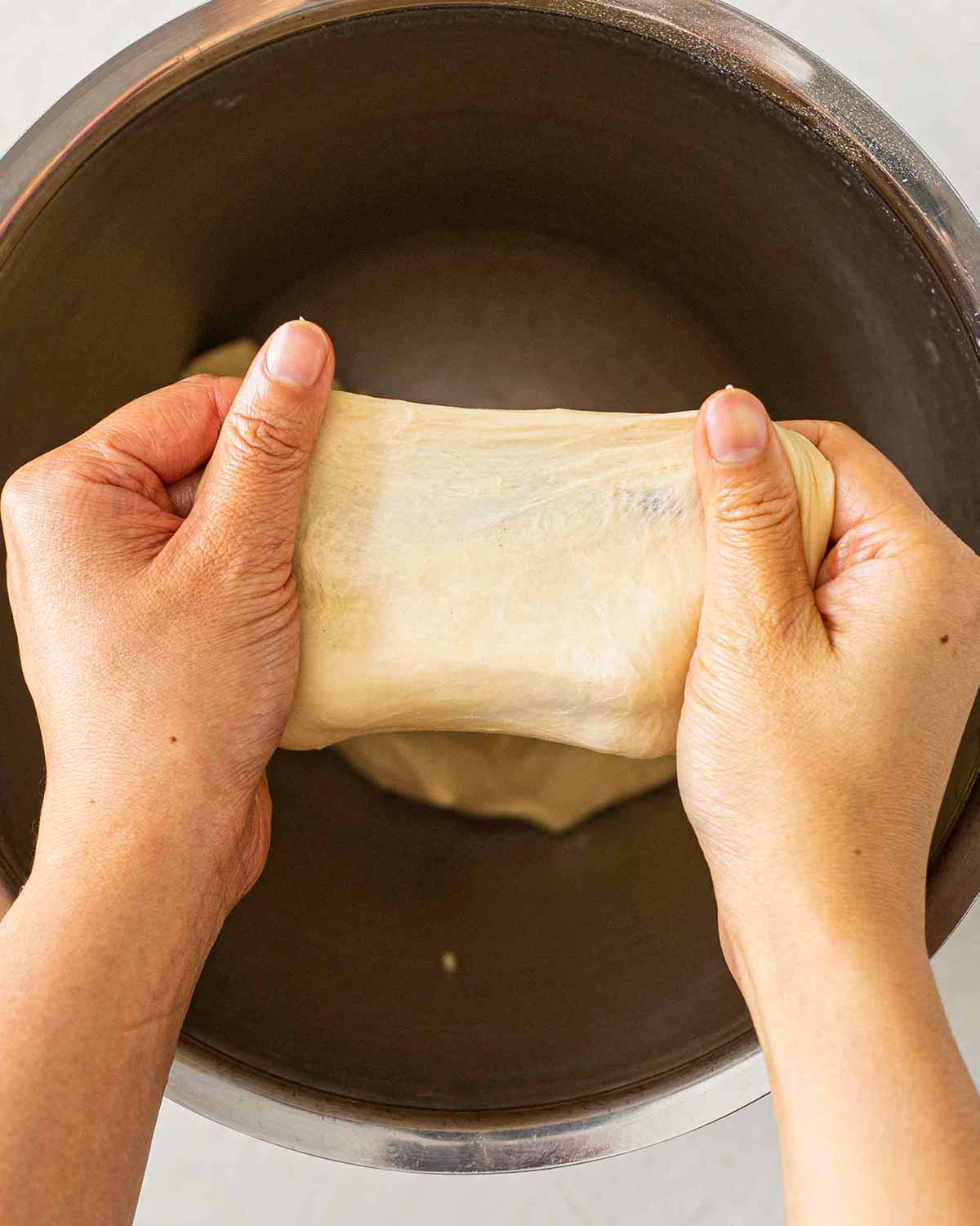 Hands stretching piece of brioche dough demonstrating window pane test.