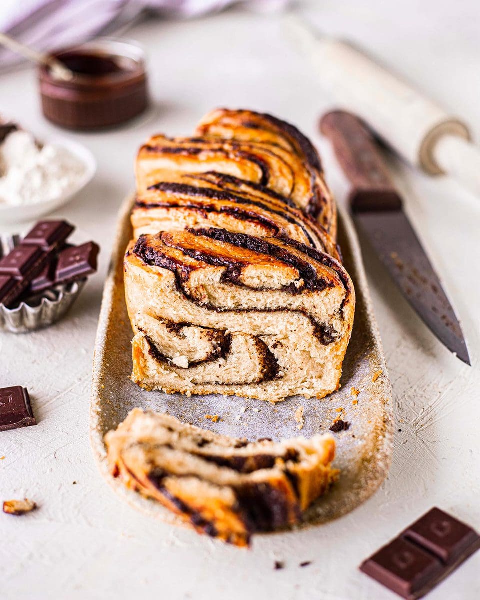 Vegan chocolate babka with slice cut off revealing swirls of ganache and brioche bread.