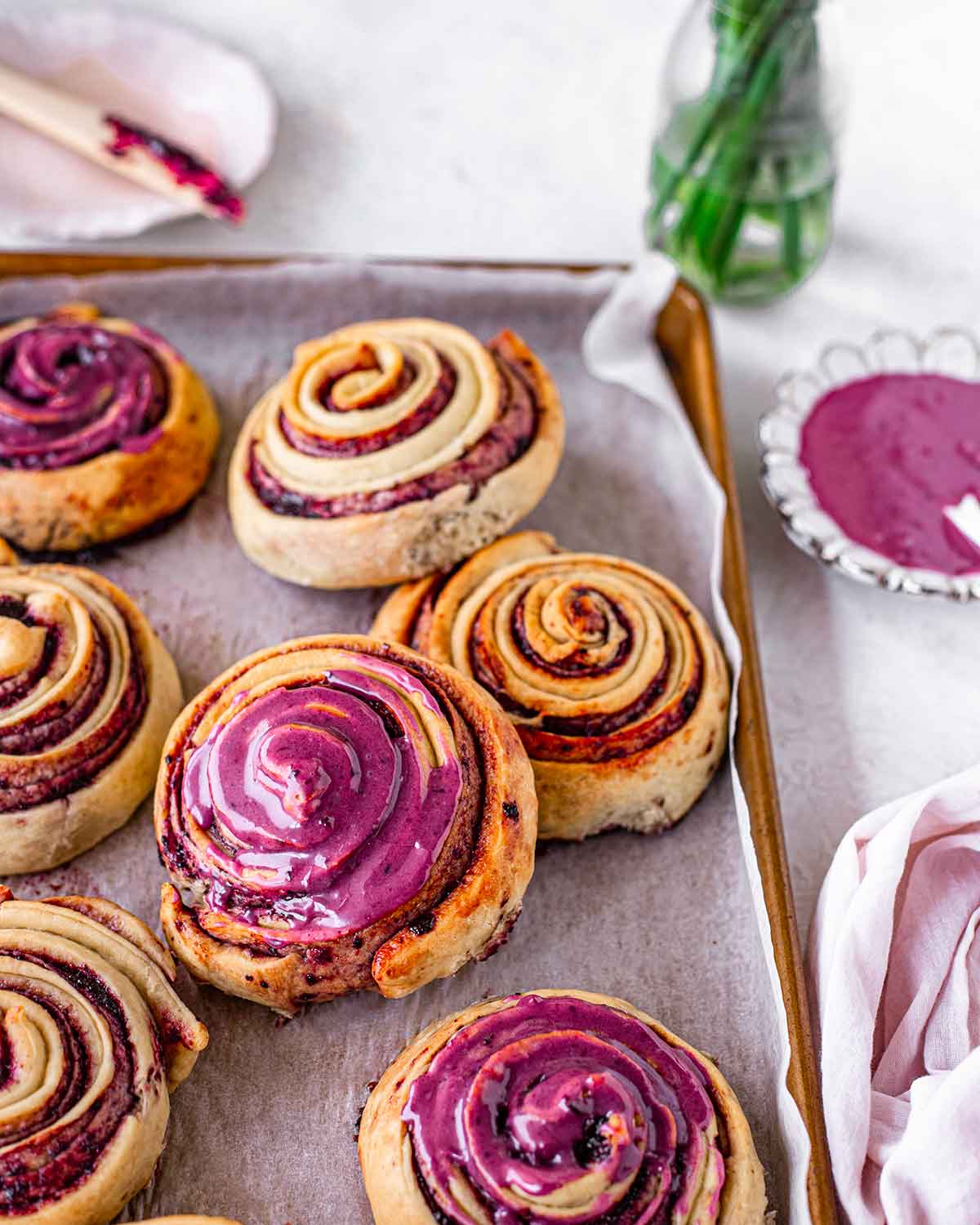 Berry rolls with vibrant icing on baking tray.