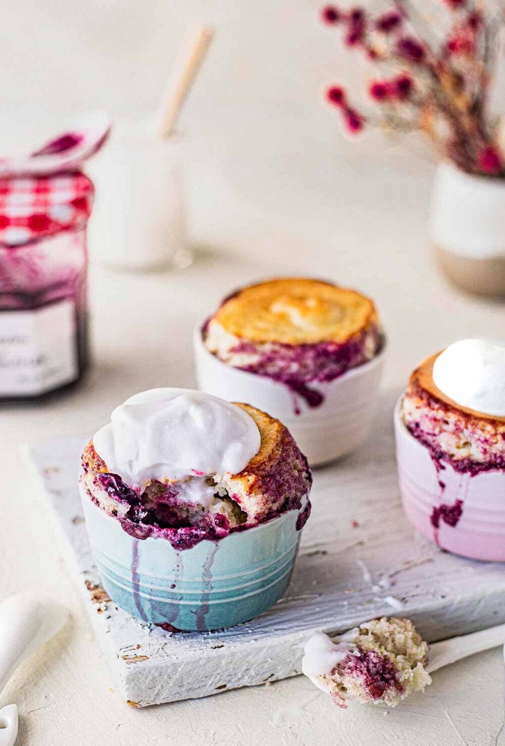 Self saucing puddings in little ramekins on white chopping board. Each pudding is bursting with jam on the sides and some are topped with yoghurt