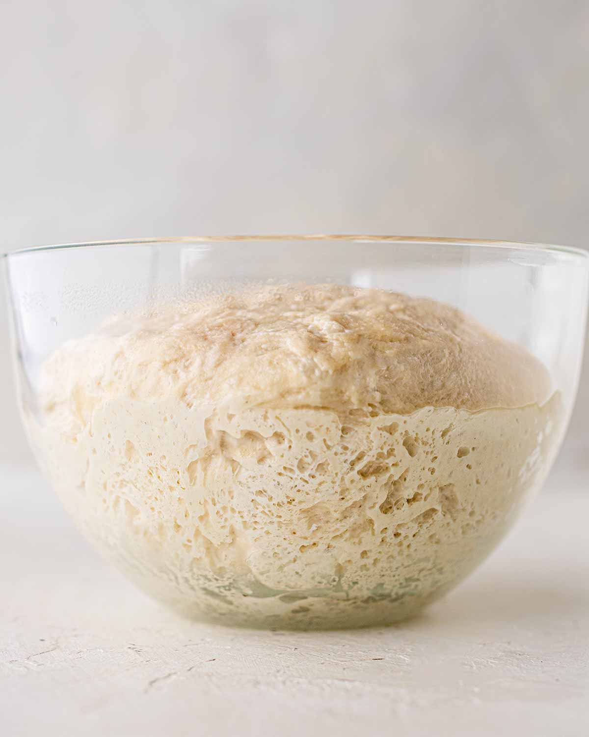 Puffy brioche dough in glass bowl showing little bubbles on the side.