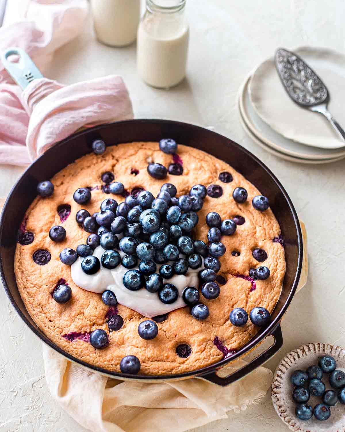 Baked vegan blueberry pancake in cast iron pan topped with coconut yoghurt.