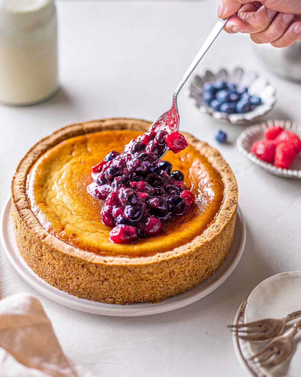 Stewed berries spooned onto naked baked cheesecake. Cheesecake has a golden surface.