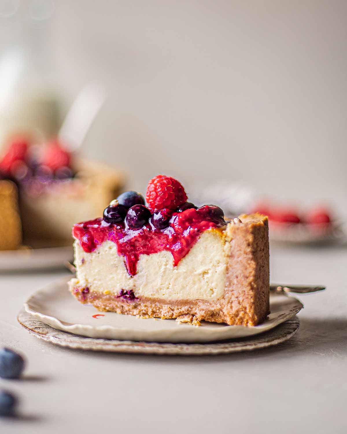 Close up of slice of baked cheesecake with berry compote dripping down the smooth filling.