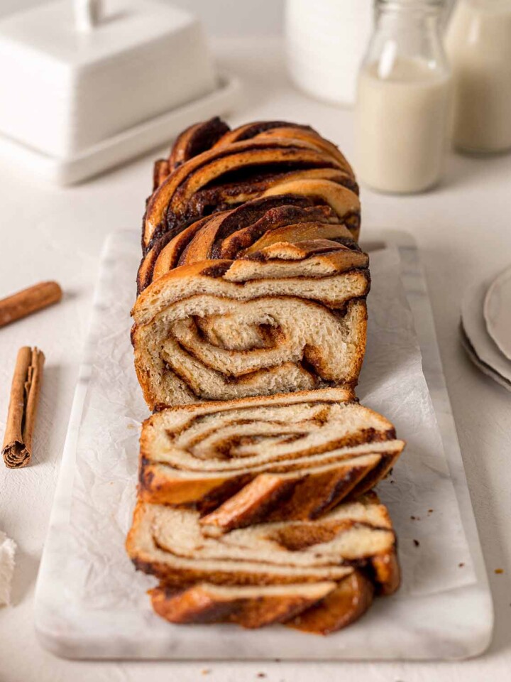 Vegan cinnamon babka on marble board with slices cut off showing inside swirl pattern.