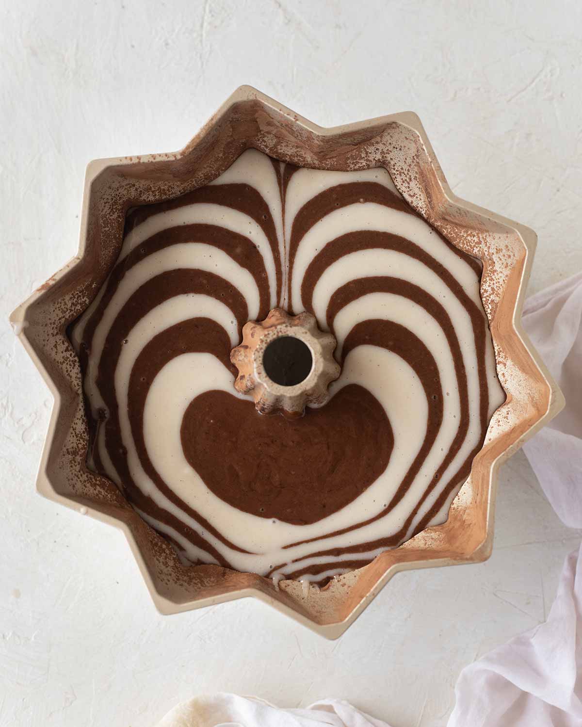Bundt tin filled with chocolate and vanilla cake batter in zebra pattern.