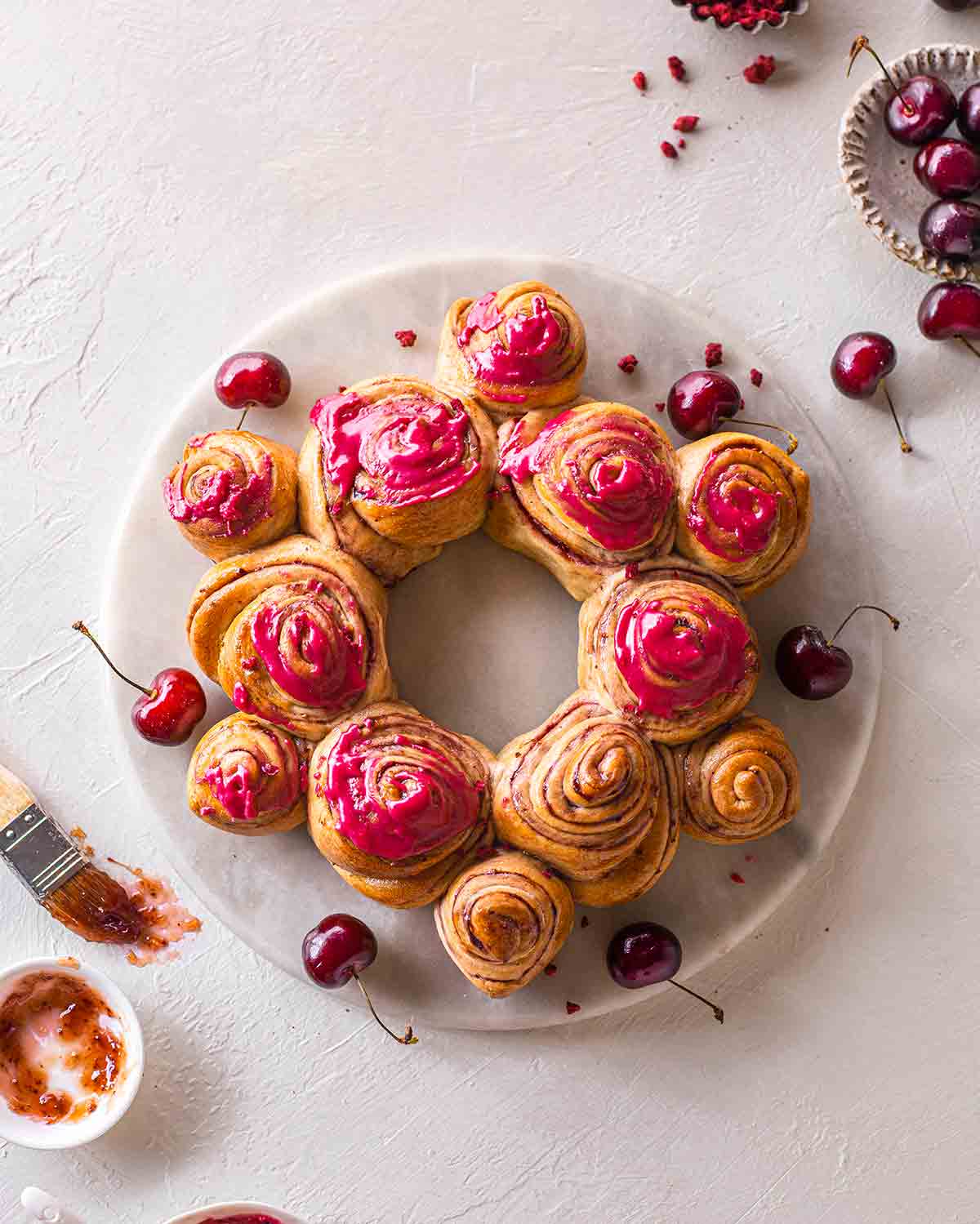 Cherry roll wreath on marble board. The wreath is partially iced with a bright pink glaze. Image shows final result of cherry wreath recipe.