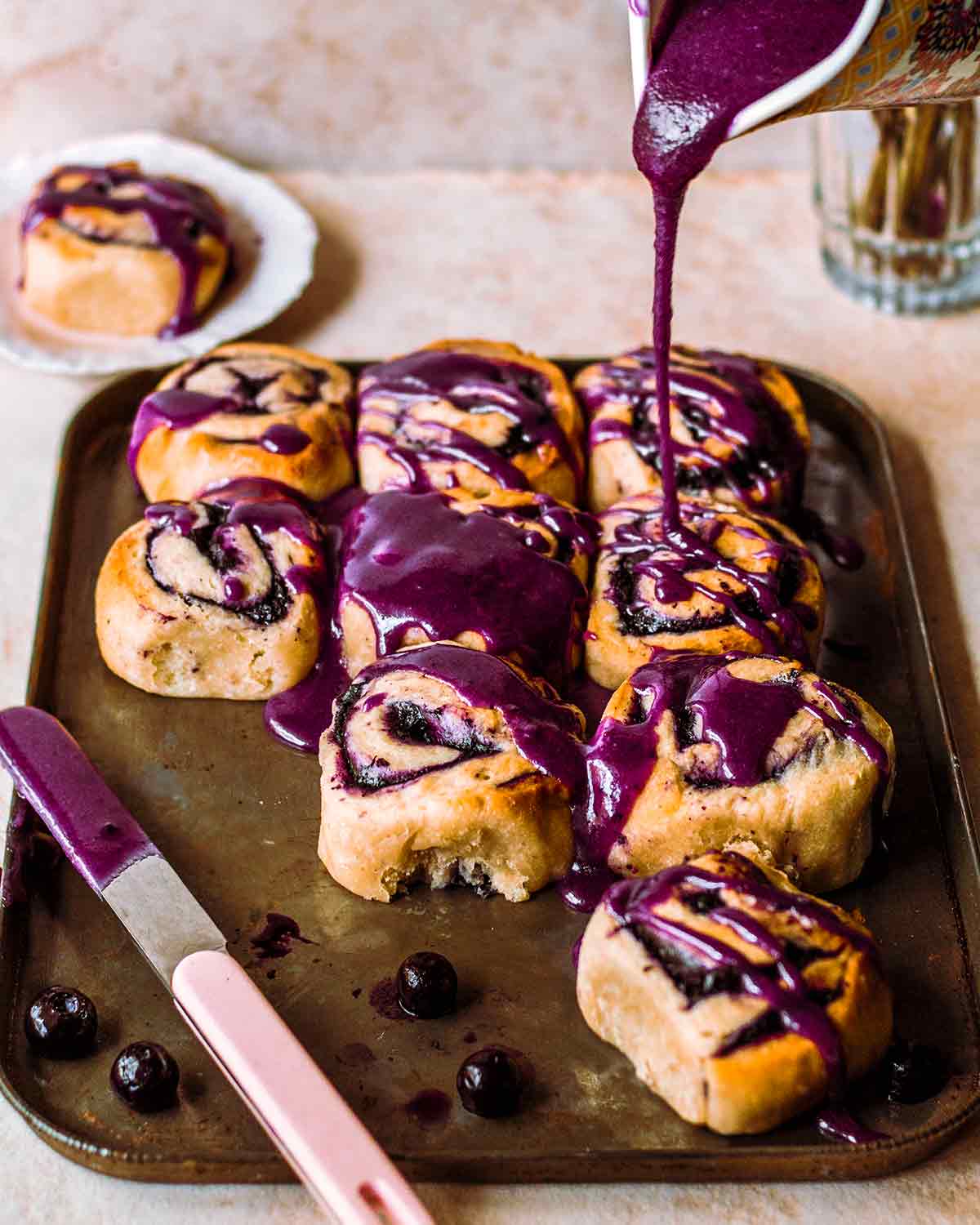 Blueberry scrolls on a tray with deep purple glaze being poured on top.