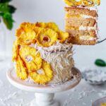 Vegan pina colada cake with slice lifted out with a cake server