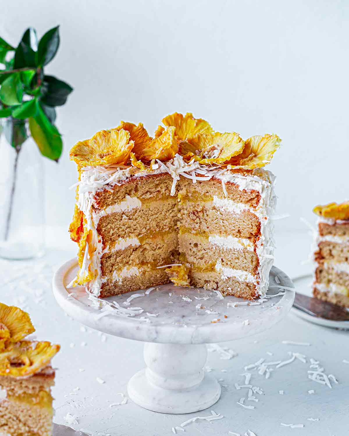 Cross section of whole vegan pina colada cake showing multiple layers of cake, pineapple puree, frosting and dried pineapple on top.