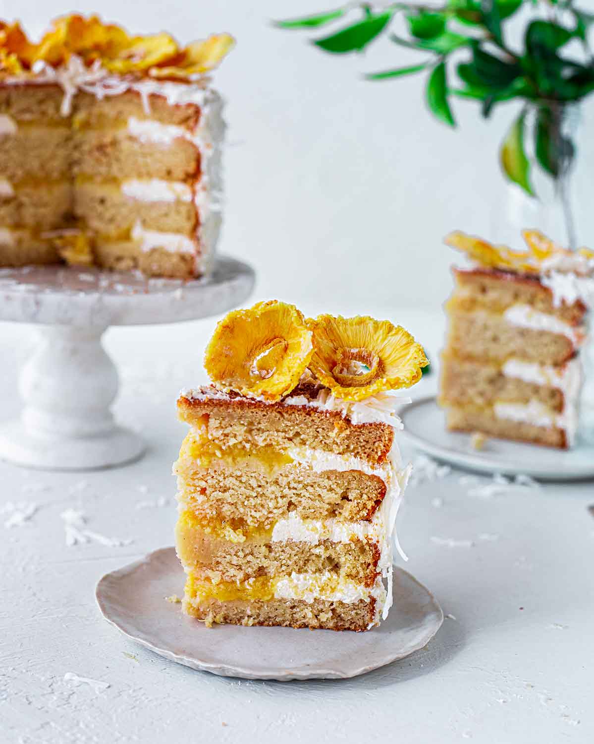 Close up of one slice of vegan pina colada cake showing multiple layers, pineapple filling and frosting.