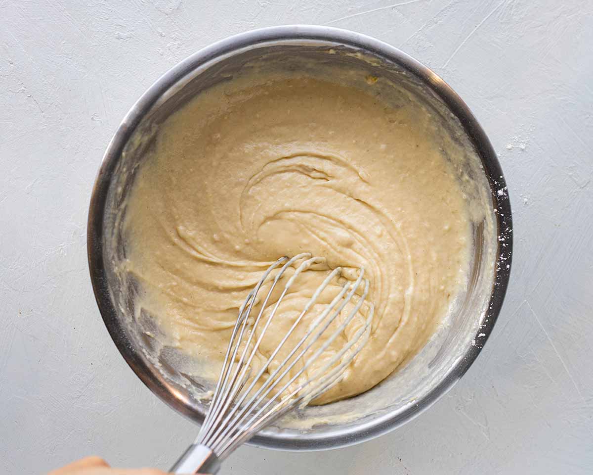 Vegan Pina Colada Cake wet batter in bowl with whisk coming out.