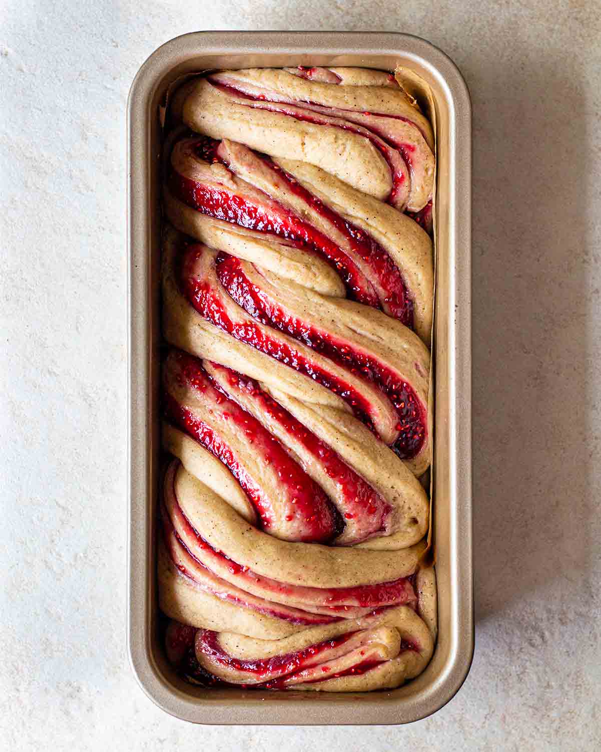 Unbaked raspberry jam donut babka in long loaf tin.