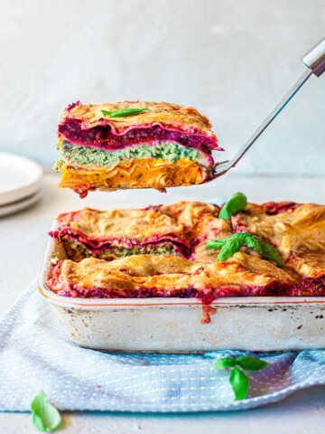 Vegan Rainbow Lasagna in casserole dish with slice lifted out revealing all the colourful layers
