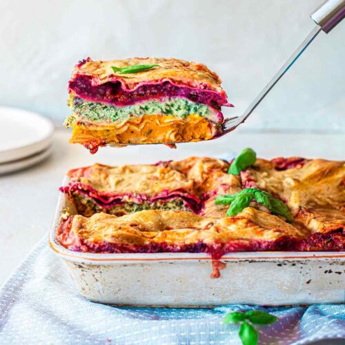 Vegan Rainbow Lasagna in casserole dish with slice lifted out revealing all the colourful layers