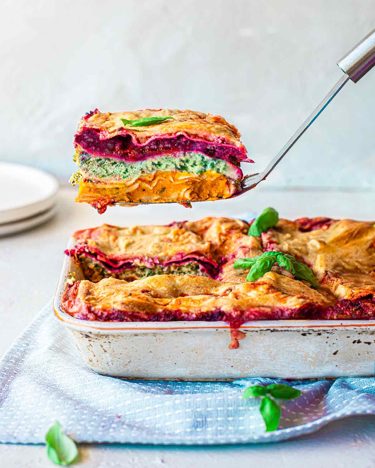 Vegan Rainbow Lasagna in casserole dish with slice lifted out revealing all the colourful layers.