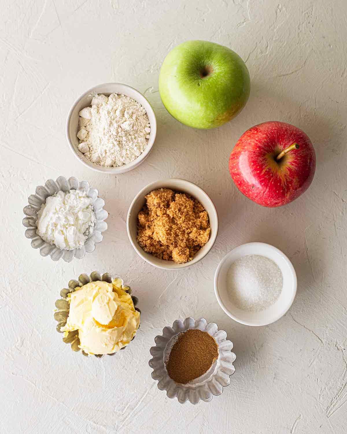 Flatlay of ingredients for vegan apple pie including: apples, flour, corn starch, brown sugar, regular sugar, vegan butter and spices