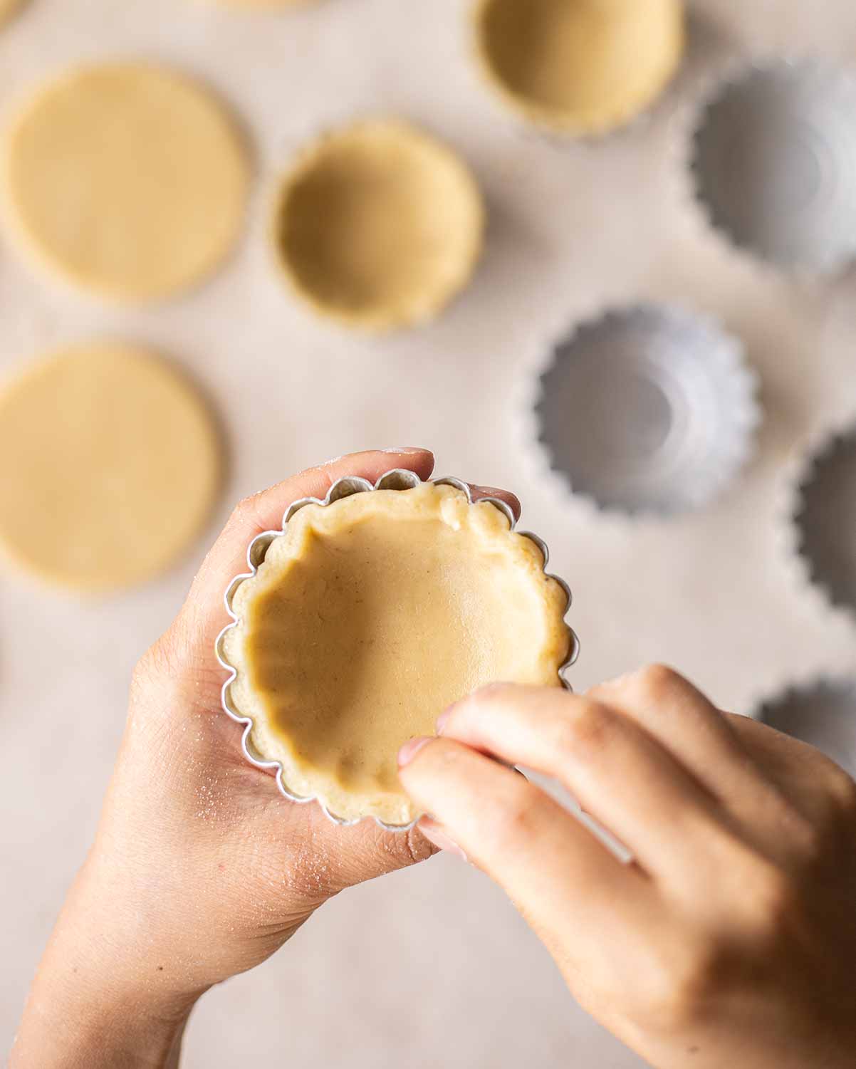 Close up of two hands pressing a round of pastry in a greased mini tart tin.