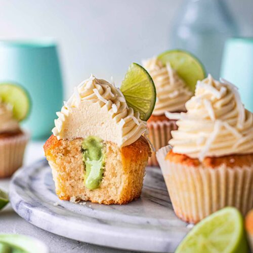 Vegan coconut lime cupcakes on marble board. One cupcake has a bite taken out of it showing the pastel green lime curd filling