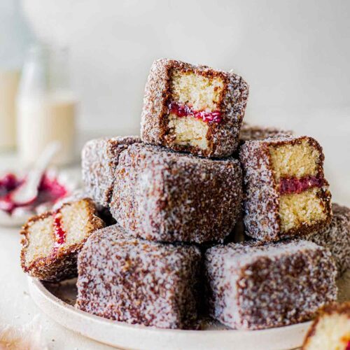 Stack of vegan lamingtons on a plate showing fluffy vanilla sponge and jam