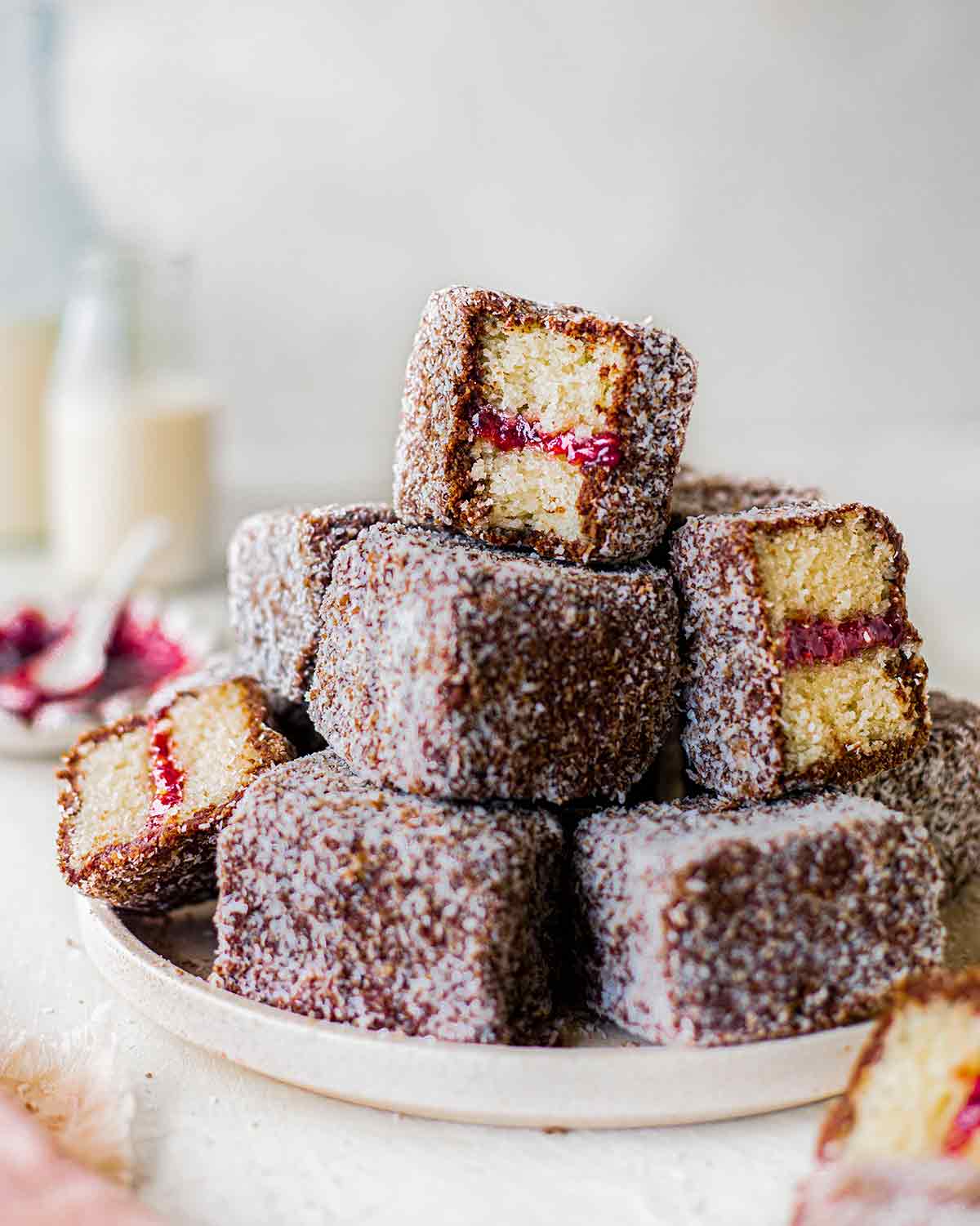 Stack of vegan lamingtons on a plate showing fluffy vanilla sponge and jam.