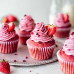 Vegan strawberry cupcakes with pink base and pink vegan buttercream. Cupcakes are decorated with freeze dried raspberries and fresh strawberries