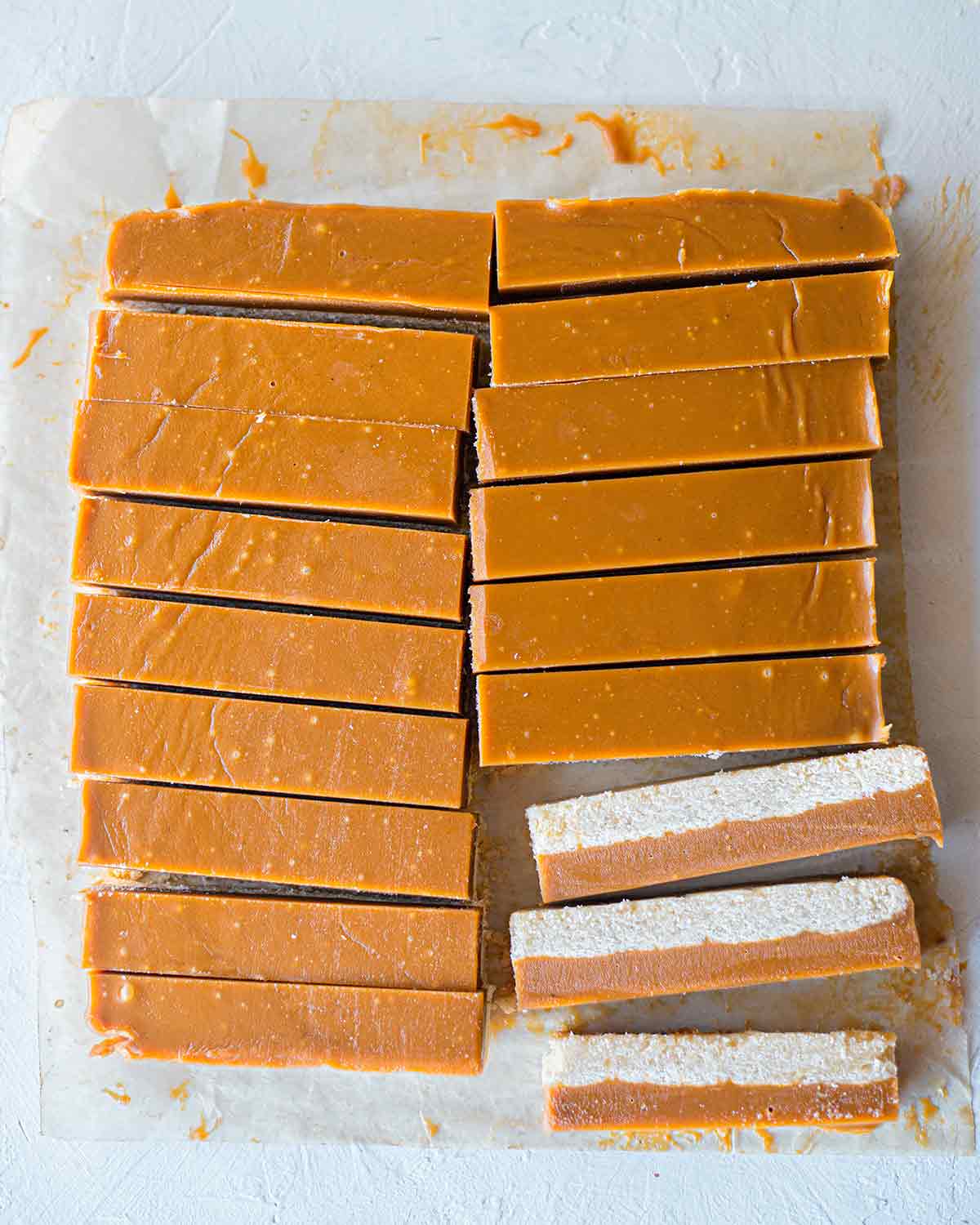 Flatlay of vegan twix bars without their chocolate coating on baking paper. Three bars are on their side showing the neat layers of cookie and caramel.