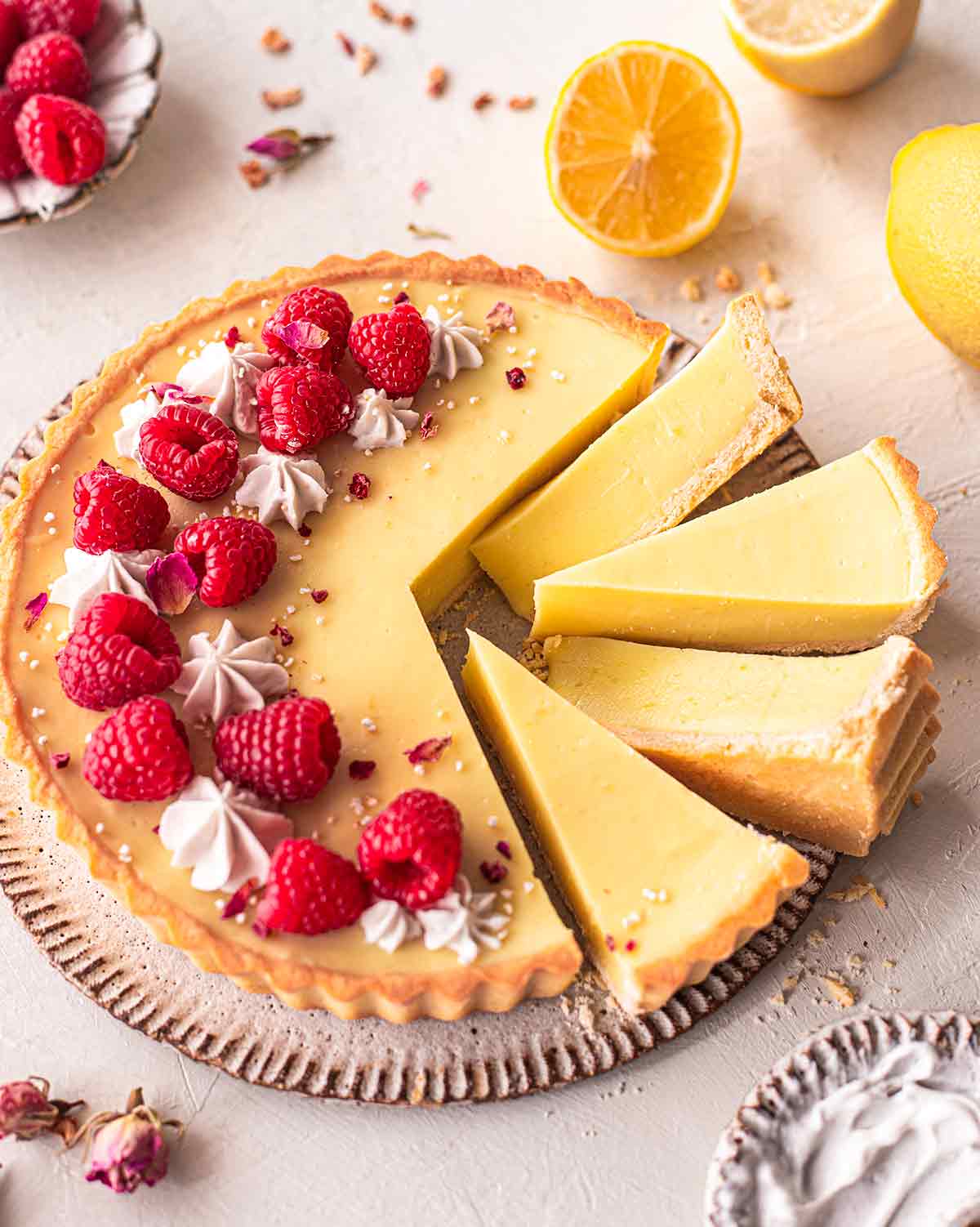 Side angle of lemon curd tart on plate with a few slices coming out showing texture.