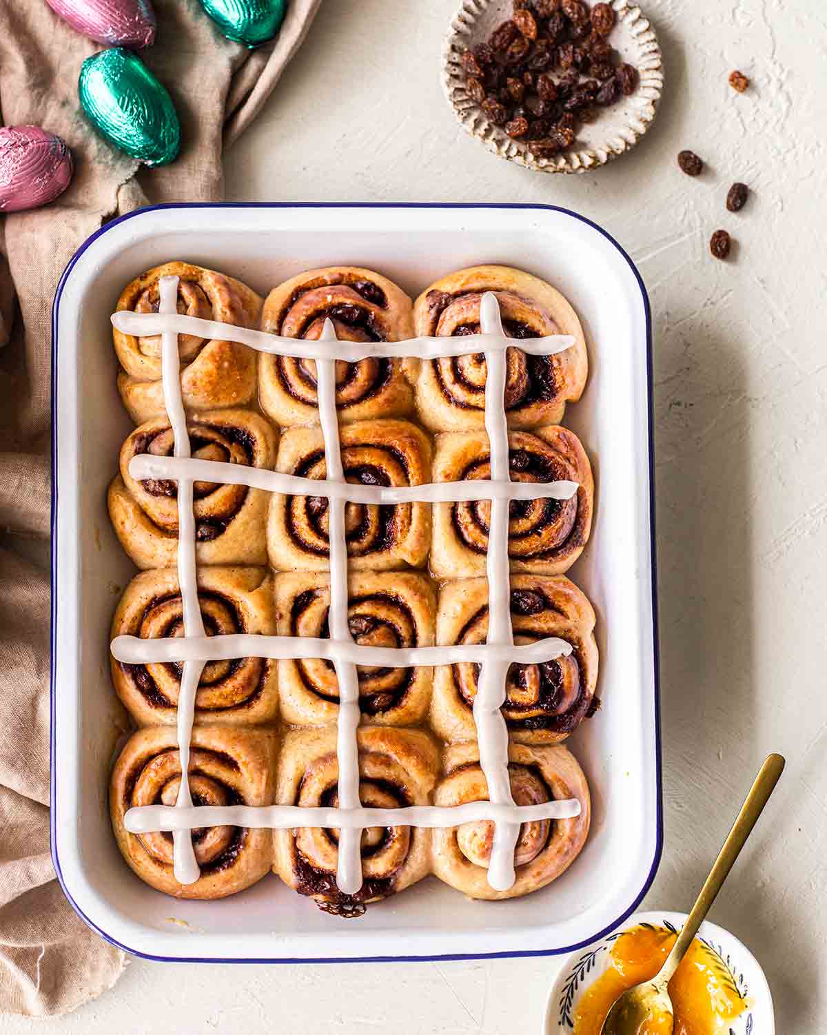 Overhead photo of hot cross cinnamon rolls in baking tray. The cross is extended from one roll to another.