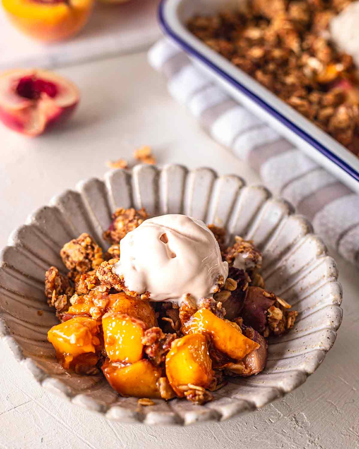 Close up of individual serving of peach crumble topped with dairy free ice cream.