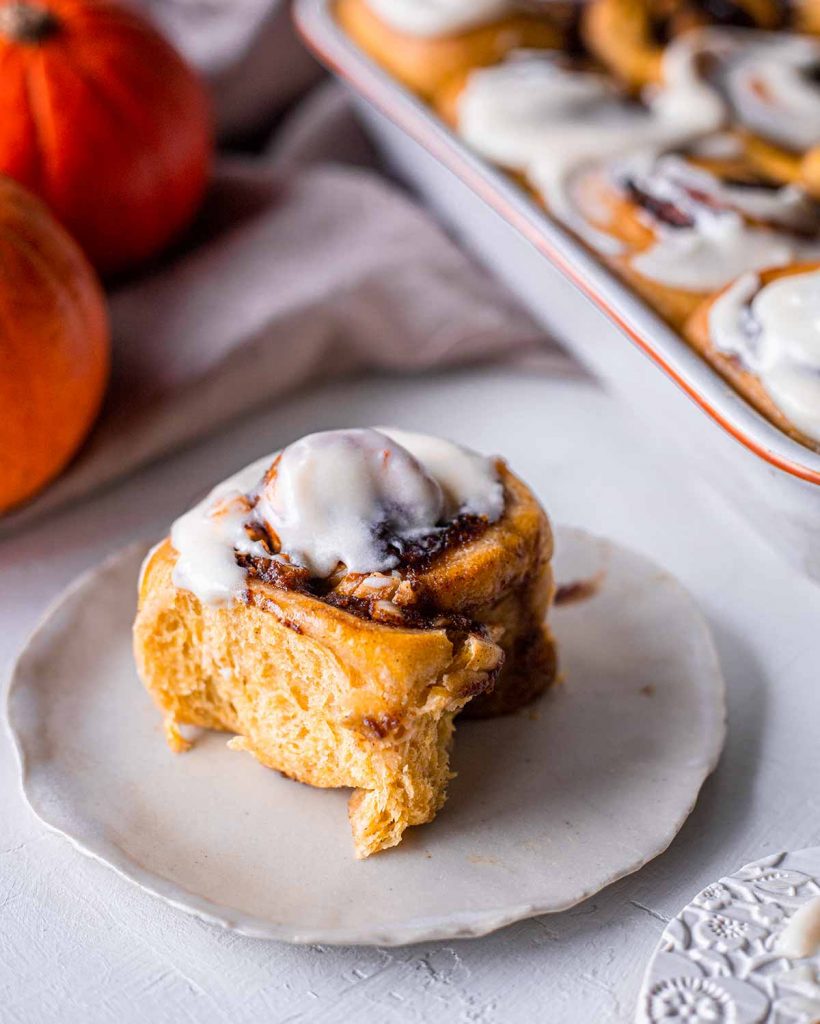 Individual pumpkin cinnamon roll with a smear of cream cheese frosting