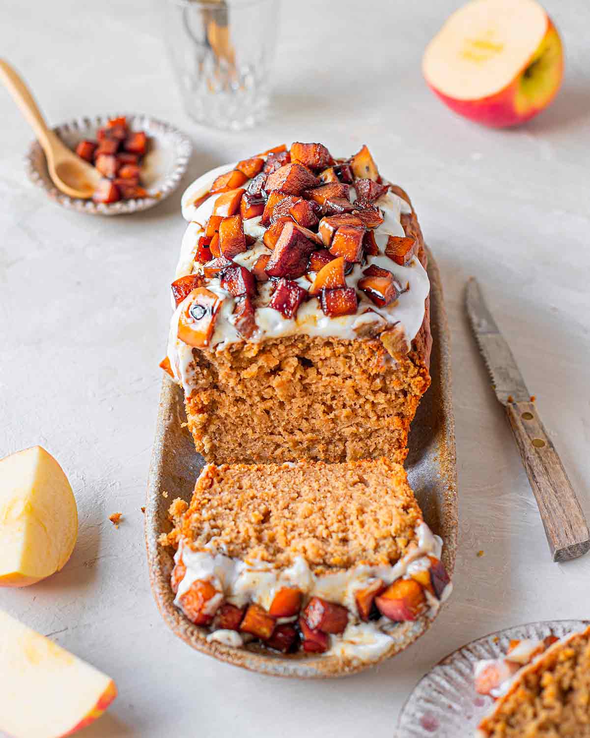Vegan apple bread topped with coconut yoghurt and caramelised apples. A slice of the vegan apple loaf is cut out showing the moist texture.