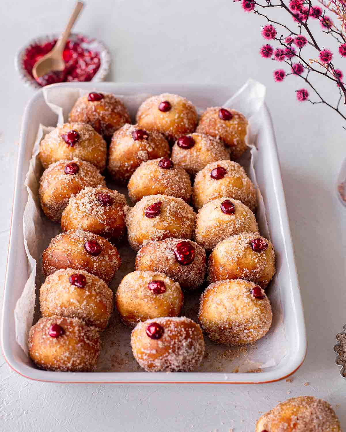 Lots of mini sugared donuts in a lined baking tray.