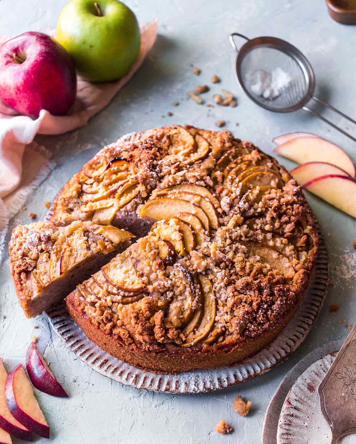 Vegan apple cake with pecan crumb topping on plate with slice coming out.