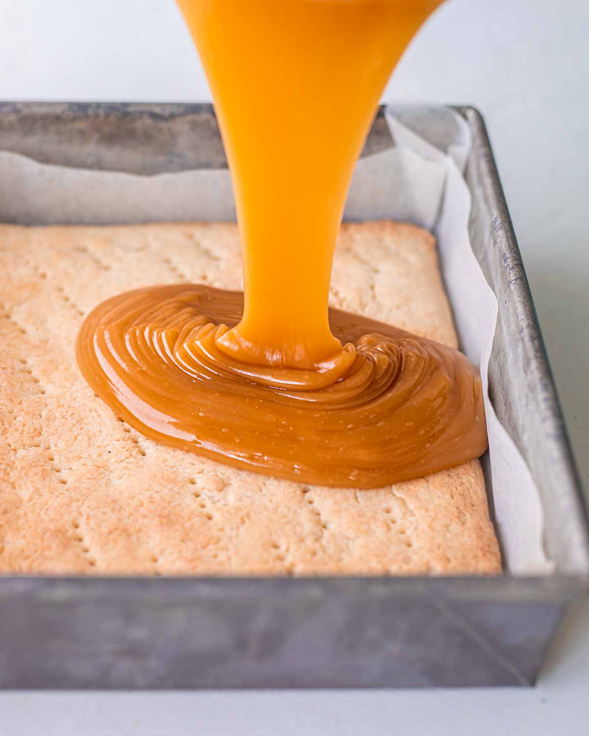 Vegan caramel being poured on baked shortcrust base.