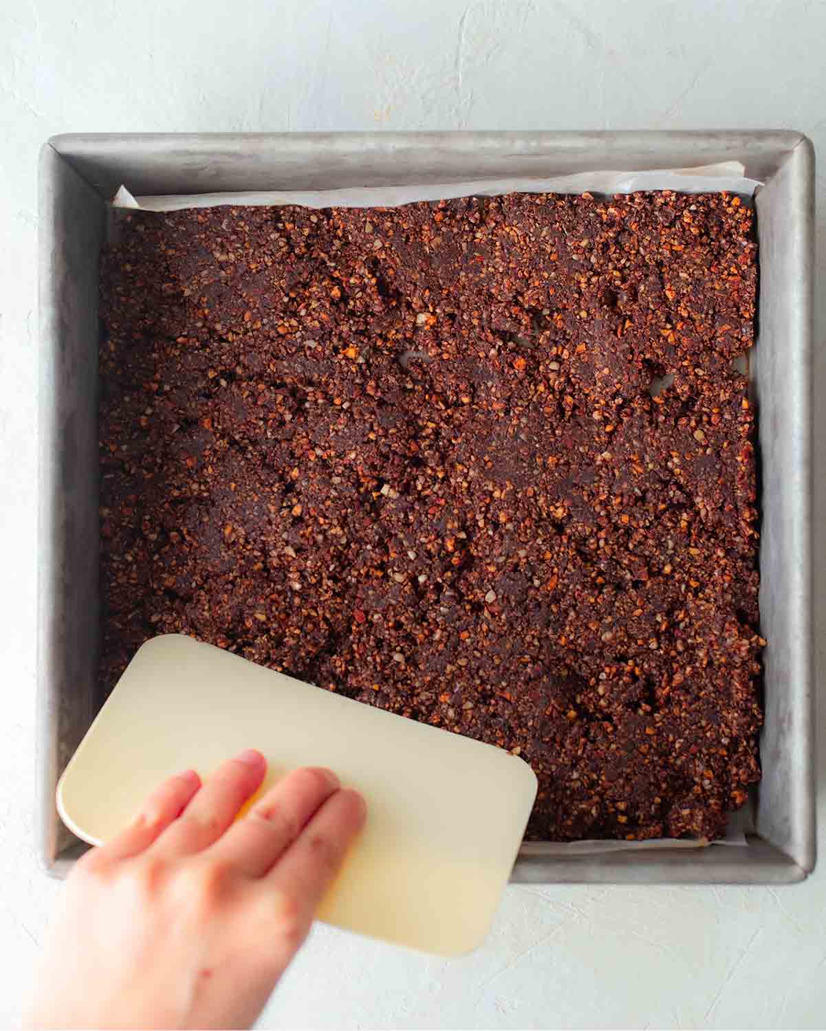 Hand pressing the chocolate layer for the vegan raspberry slice.