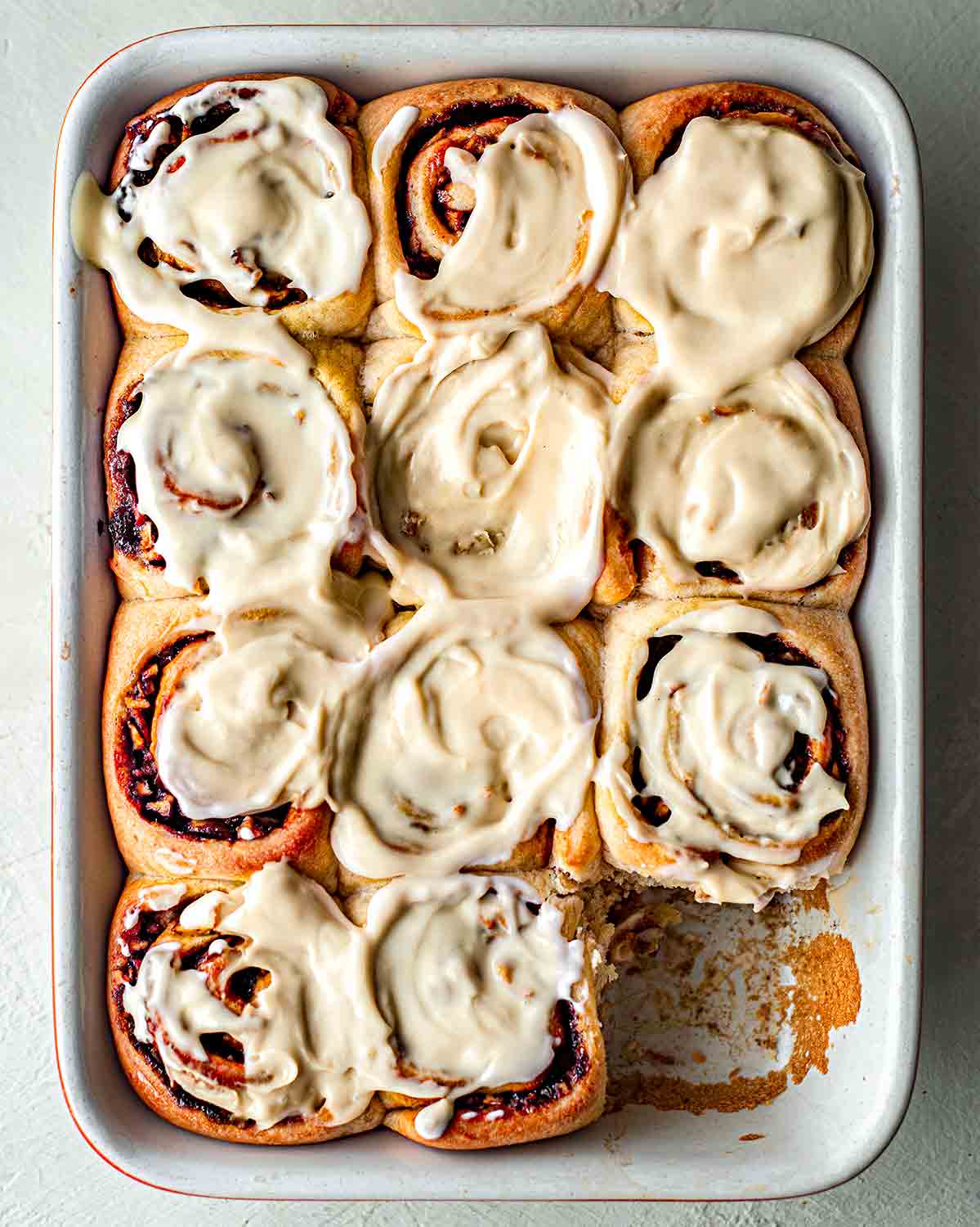 vegan apple cinnamon rolls in baking tray and lush coconut custard topping.