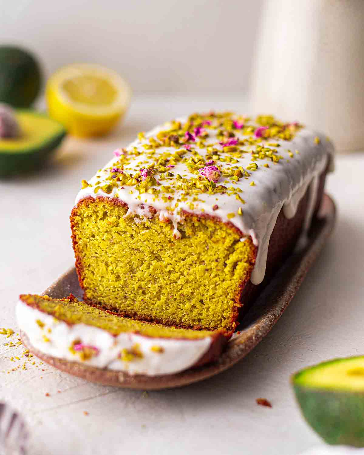 Vegan pistachio cake on rustic platter with ingredients in foreground and background.