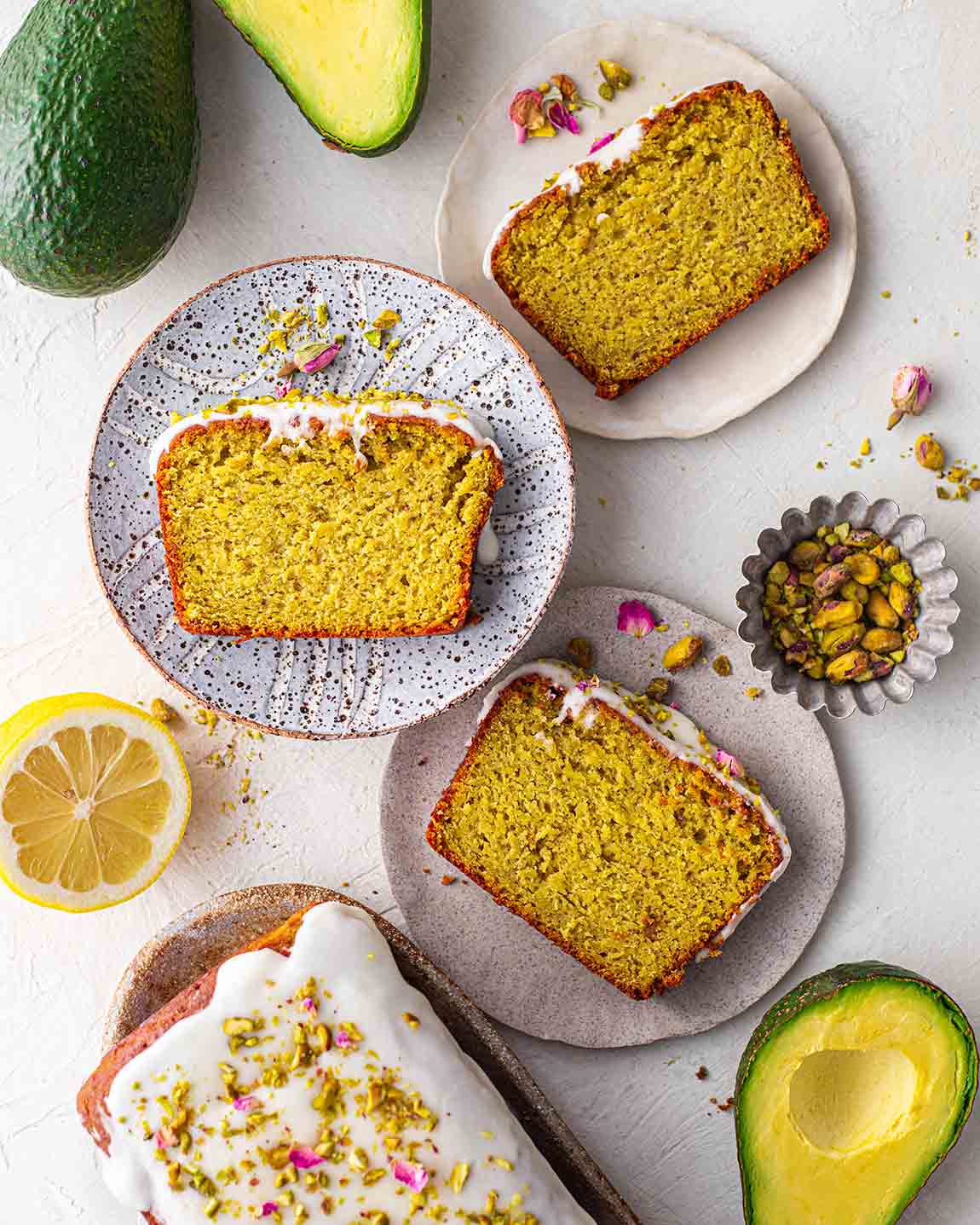 Flatlay of pistachio cake slices on rustic plates with ingredients on the sides.