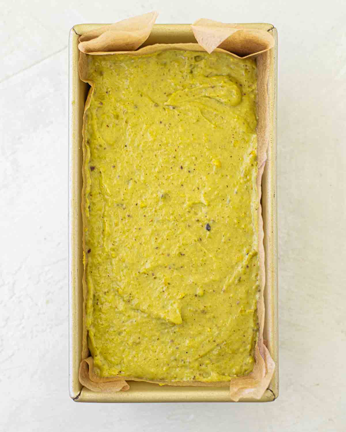 Unbaked pistachio cake in lined baking tin.