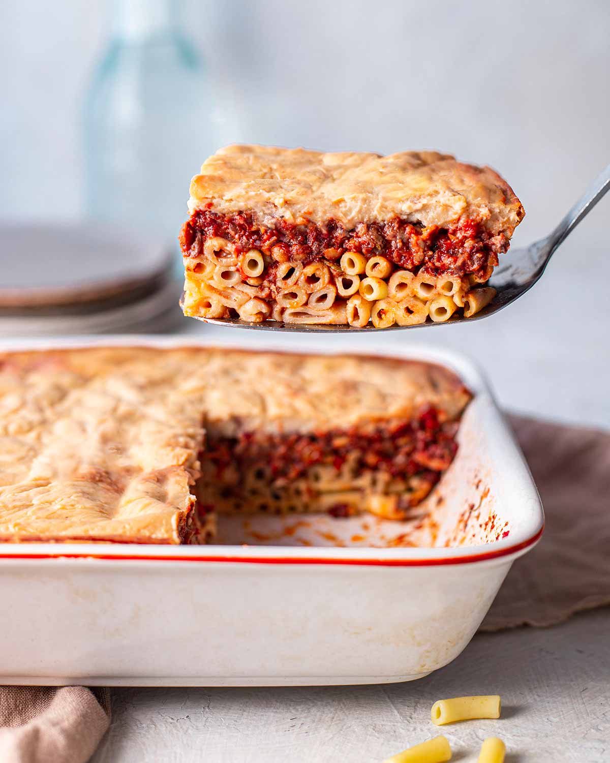 Slice of pastitsio lifted out of casserole dish revealing layers.