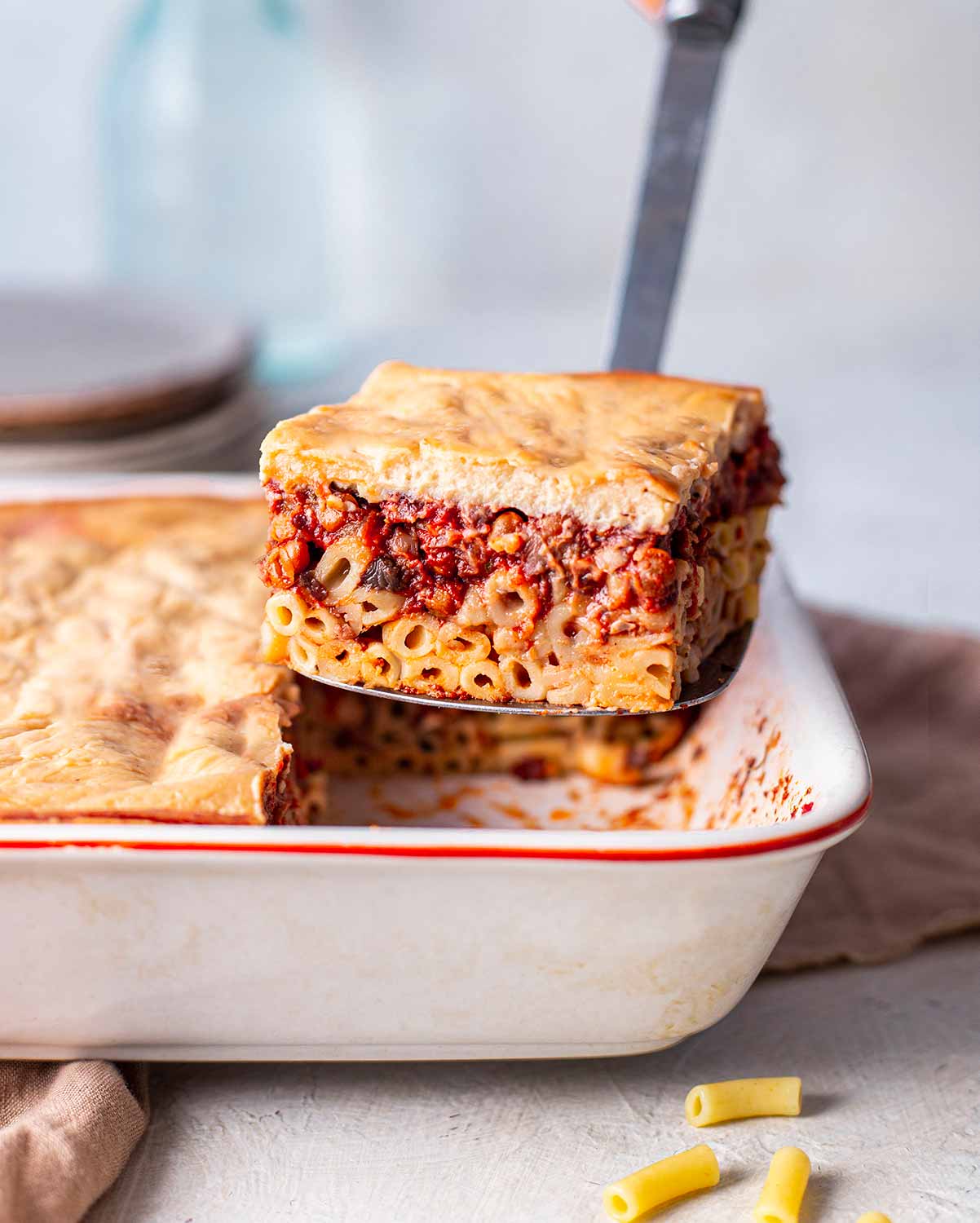 Slice of pastitsio lifted out of casserole dish revealing layers.