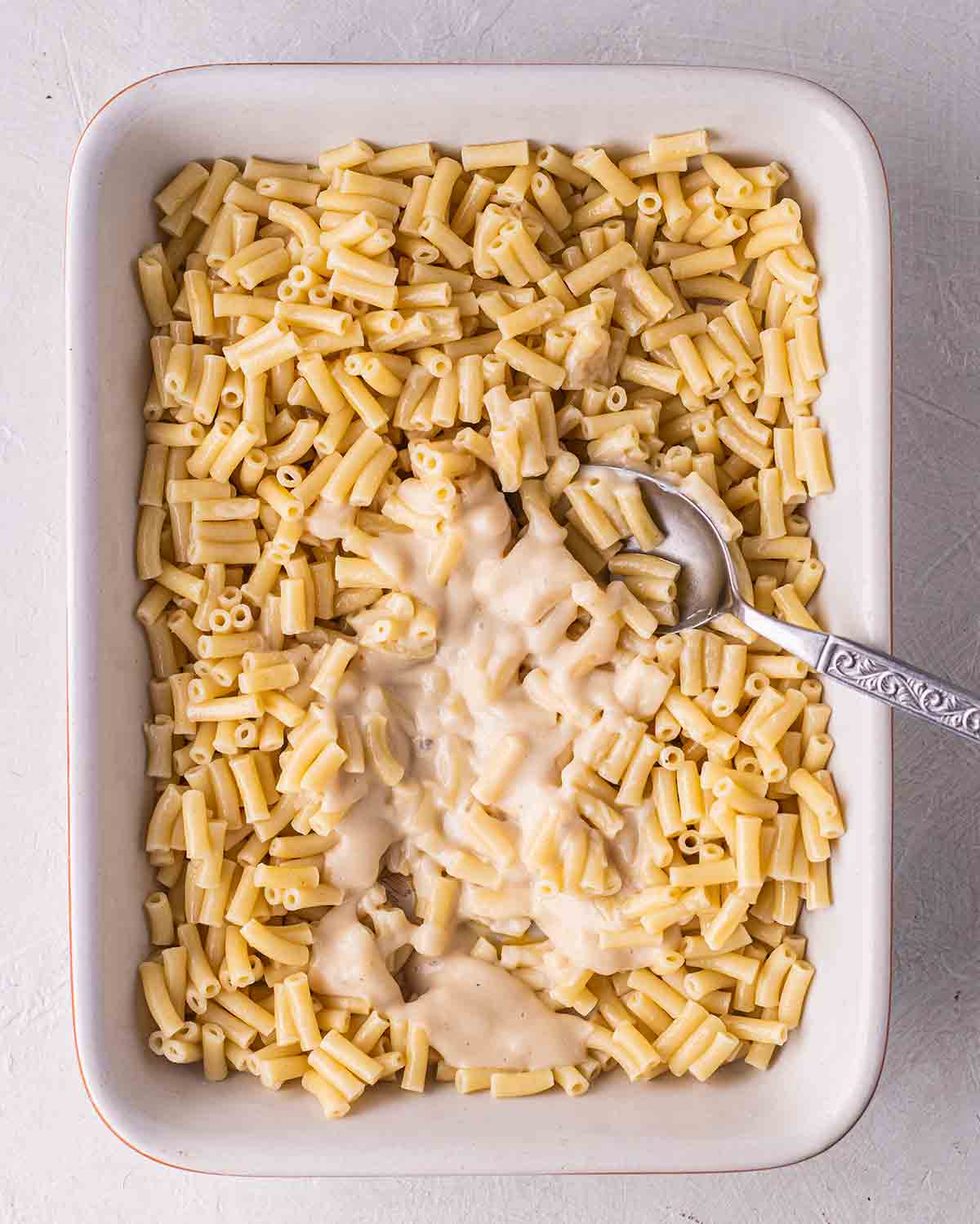 Pouring the vegan bechamel sauce onto the pasta in casserole dish.